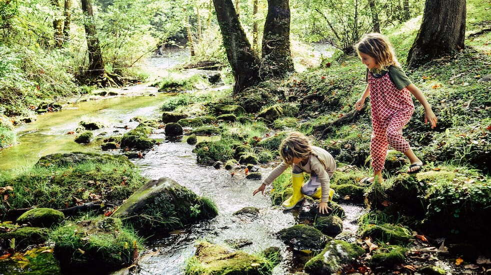 Two children having an adventure, climbing and stepping in a river exploring a beautiful natural area